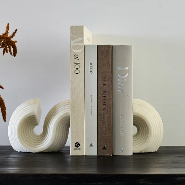 Three books on a shelf with decorative white s curve french country bookends against a plain wall.