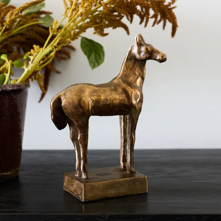 Bronze french country horse statue on a dark surface with a plant in the background