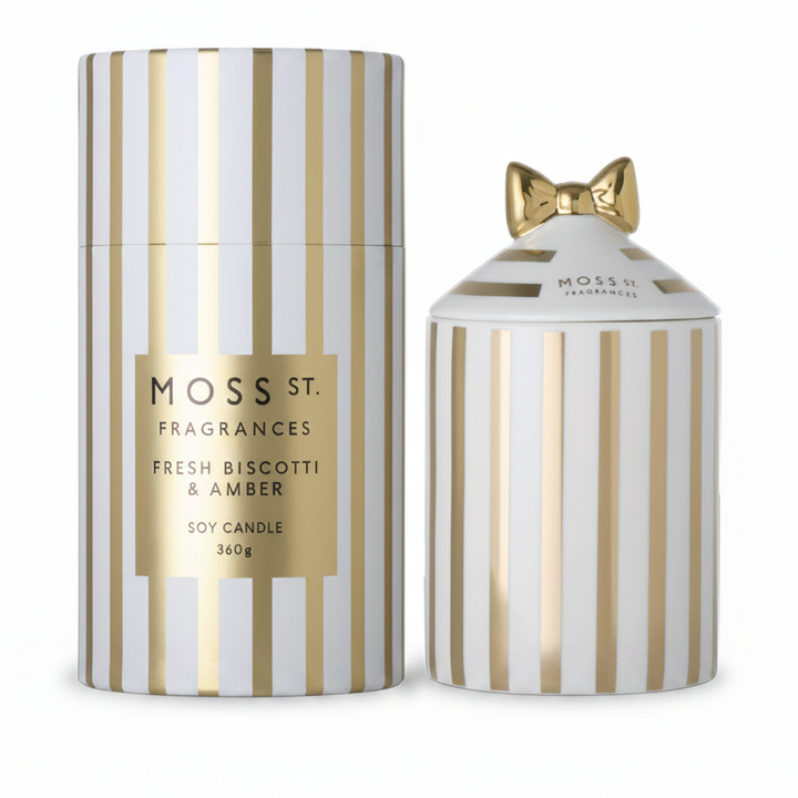 Moss St. Fragrances Fresh Biscotti & Amber soy candle set, featuring a tall cylindrical box and a smaller matching jar with a gold bow on the lid, both decorated with vertical gold and white stripes.