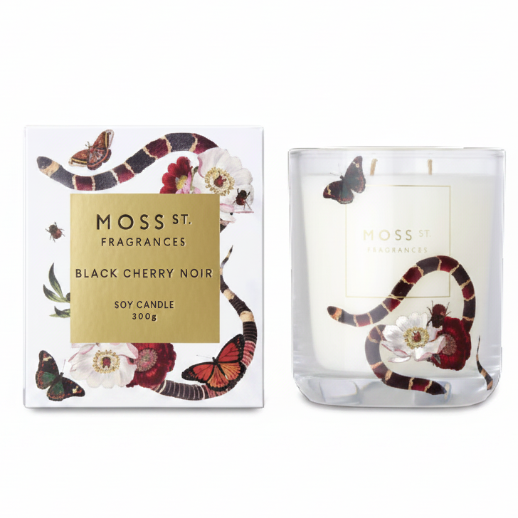 Moss St. Fragrances Black Cherry Noir soy candle shown next to its white packaging box, both decorated with a black and red snake, butterflies, and cherry blossom flowers.