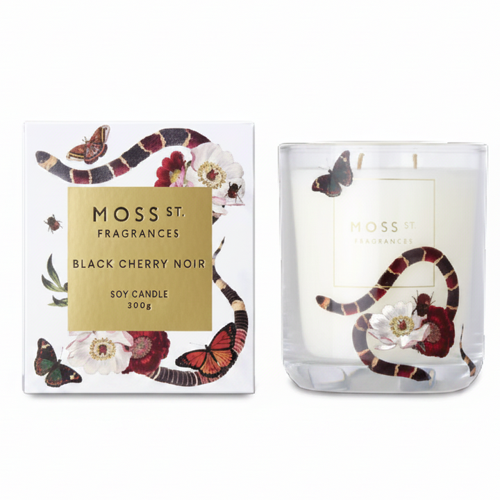 Moss St. Fragrances Black Cherry Noir soy candle shown next to its white packaging box, both decorated with a black and red snake, butterflies, and cherry blossom flowers.