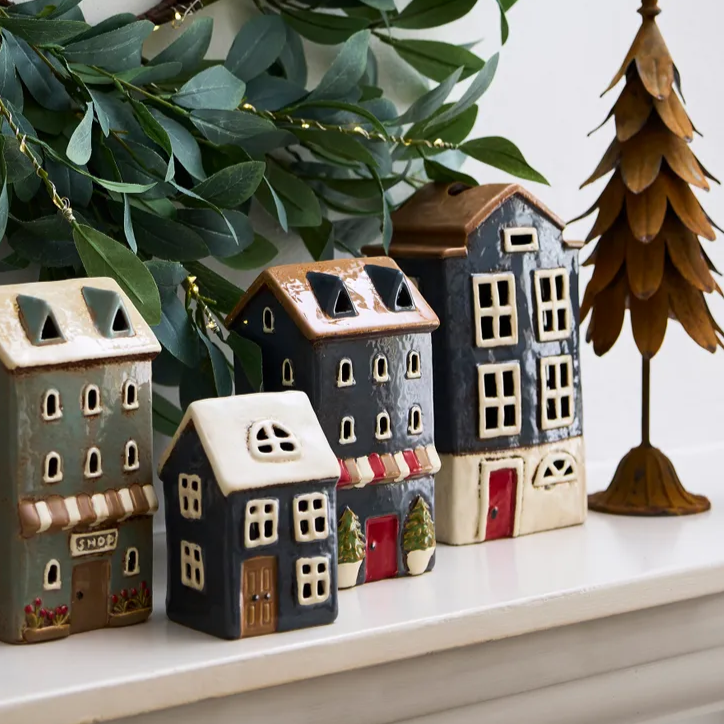 Set of small ceramic houses on a shelf with greenery and a wooden tree decoration.