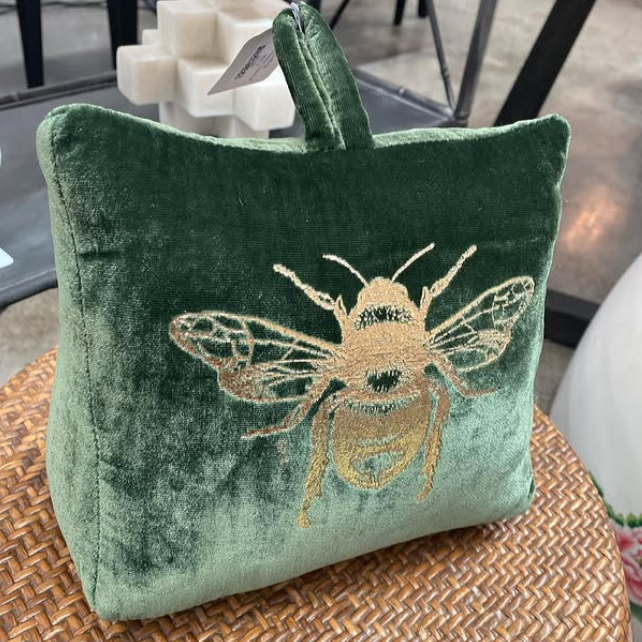 Green velvet doorstop with a gold bee design on a woven surface