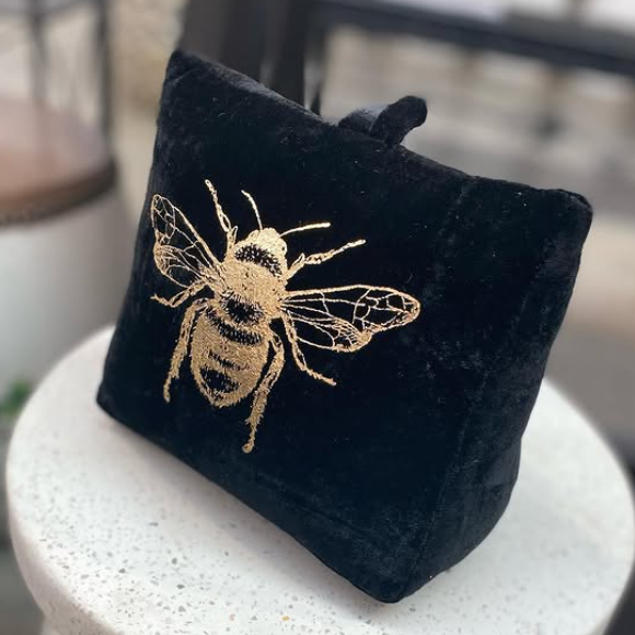 Black doorstop with a gold embroidered bee design on a white pedestal.