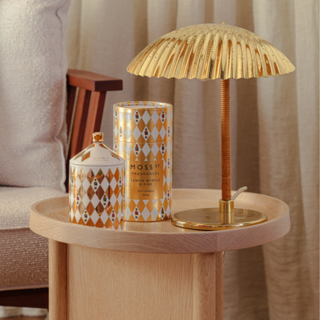Small wooden table with a decorative lamp and MOSS ST candle against a neutral curtain background