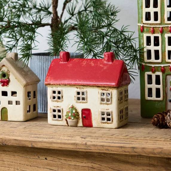 Decorative ceramic houses on a wooden surface with a Christmas tree in the background.