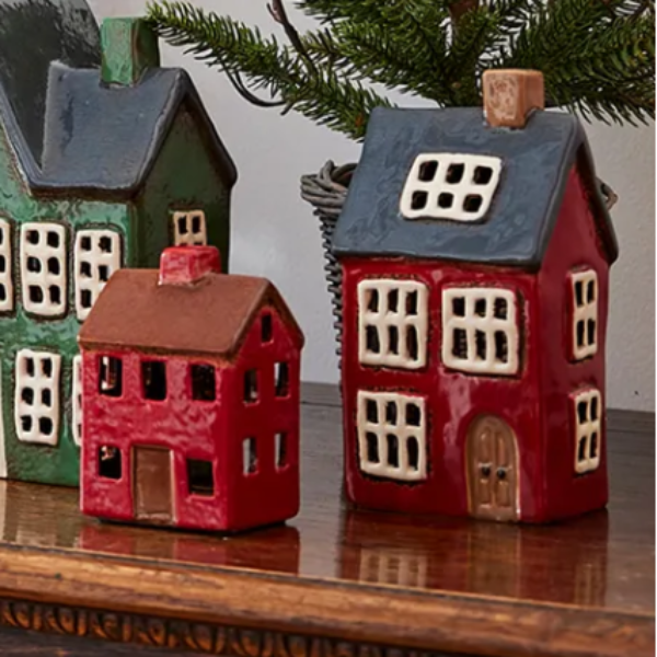 Set of miniature ceramic houses on a wooden surface with a Christmas tree in the background.
