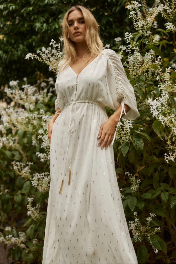 Woman in a white dress standing in front of green foliage