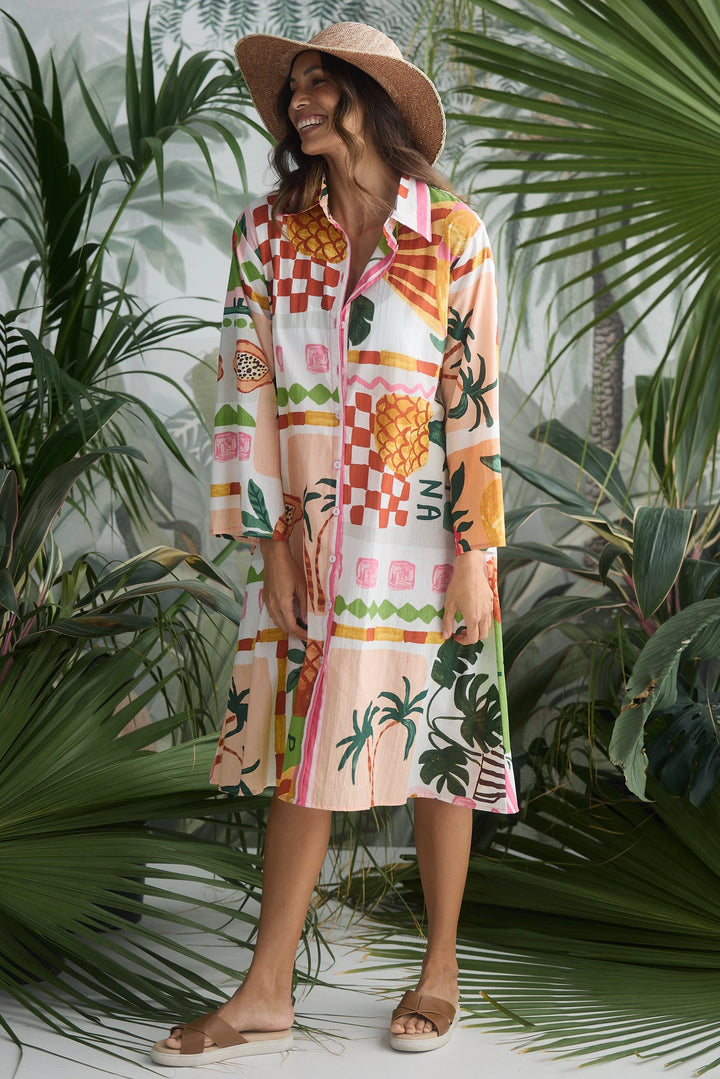 Woman in a colorful dress and hat standing among tropical plants