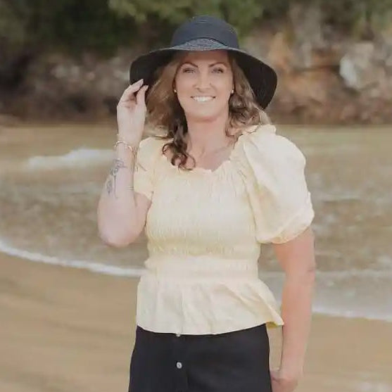 Woman standing on a beach wearing a yellow top and black skirt.