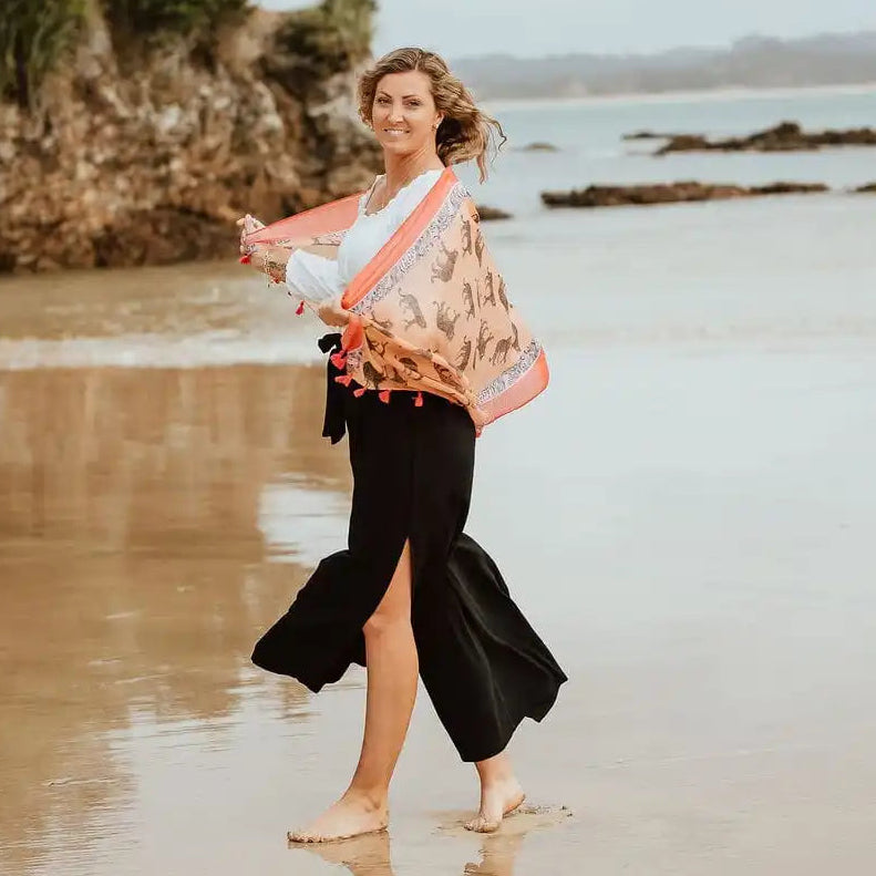 Woman on a beach holding a patterned scarf