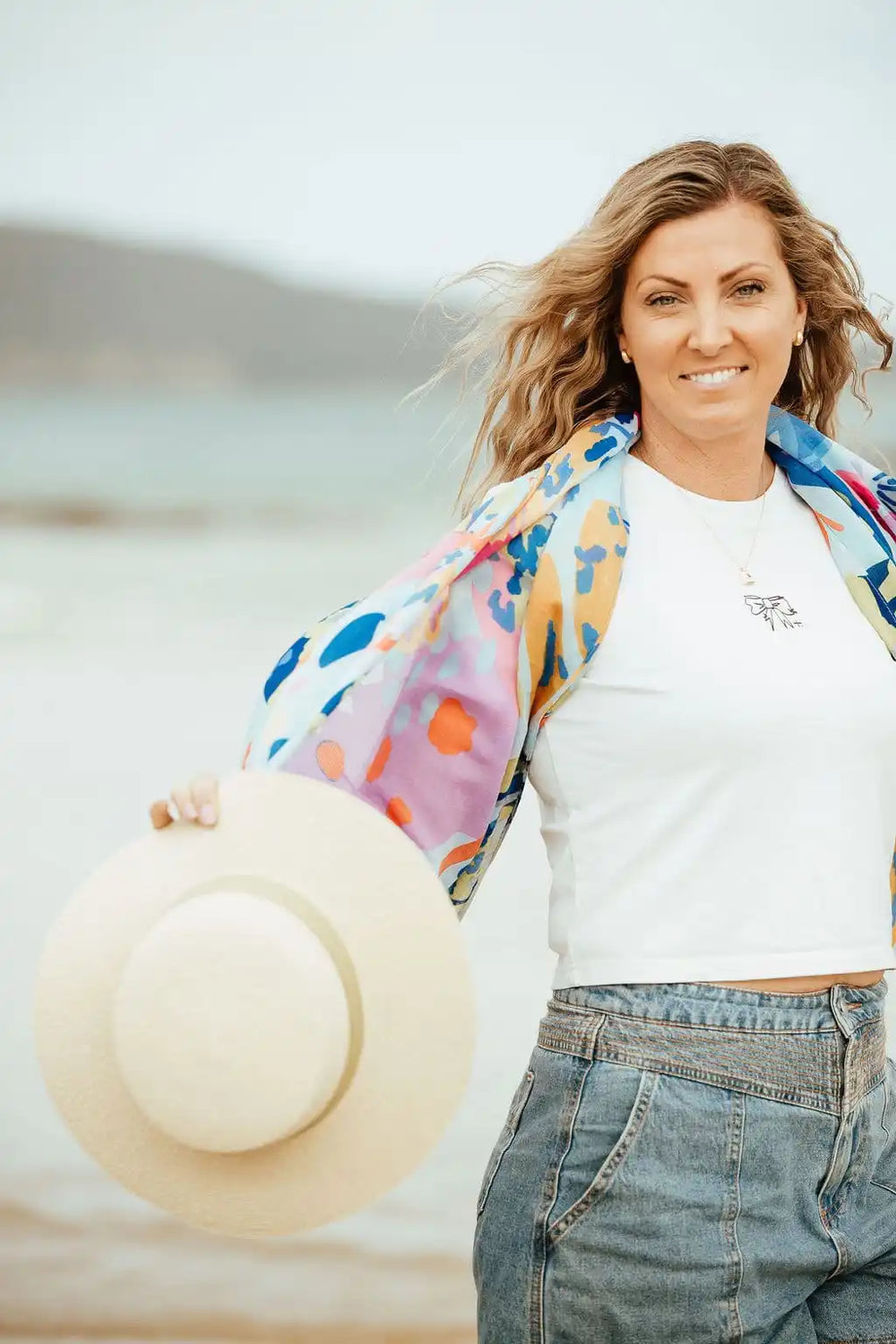Woman holding a hat on a beach with a blurred background