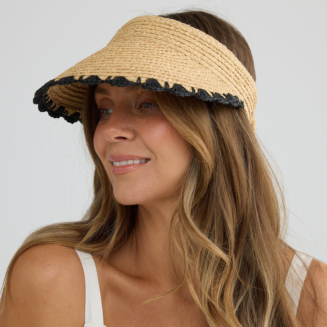 Woman wearing a straw visor with black trim on a plain background