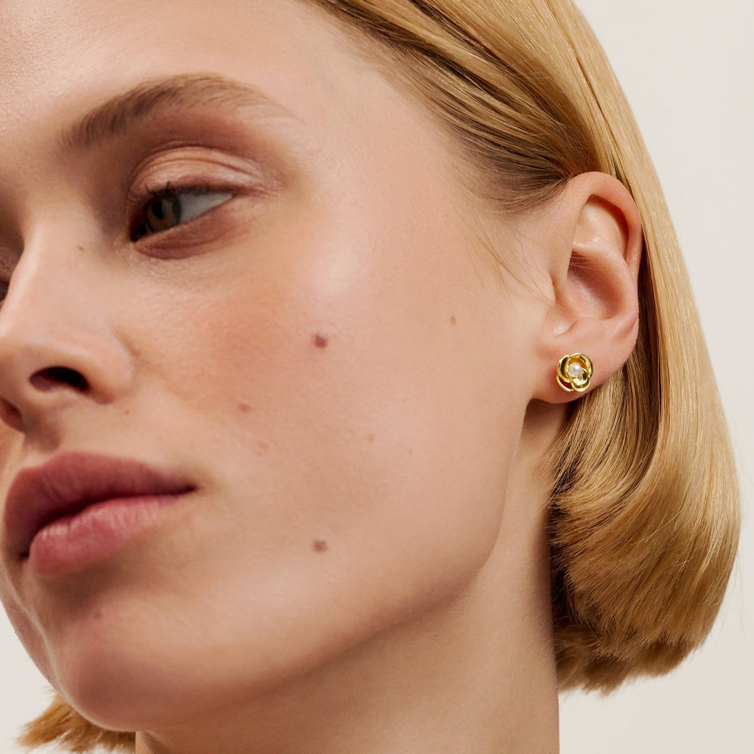 Close-up of a person wearing gold ted baker earrings against a neutral background