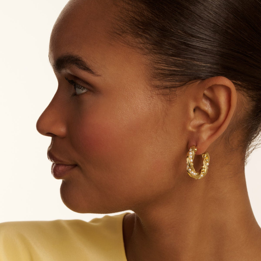 Close-up of a person wearing gold TED BAKER hoop earrings with a neutral background