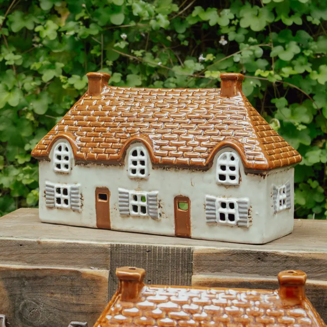 Ceramic cottage figurine with a thatched roof on a wooden surface with green foliage in the background