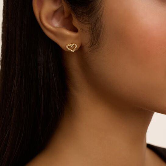 Close-up of a person wearing gold ted baker heart-shaped earrings.