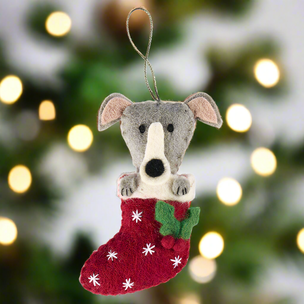 Felted animal ornament of a dog with a red stocking on a white background