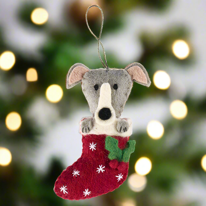 Felted animal ornament of a dog with a red stocking on a white background