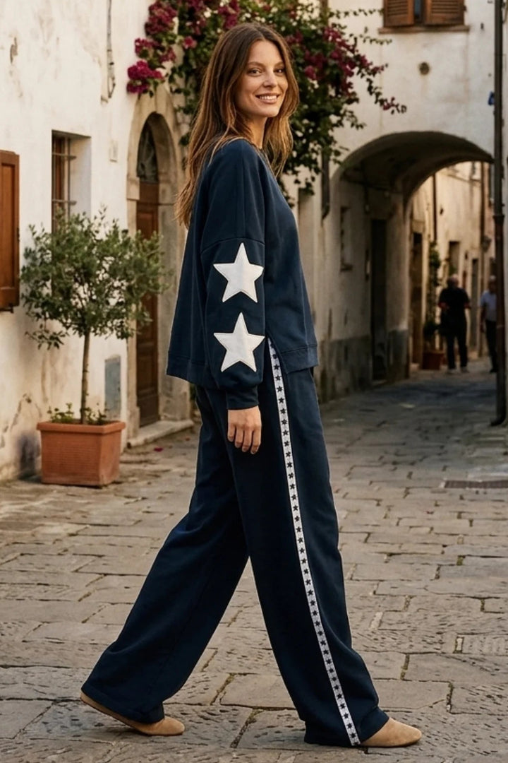 Woman in a navy blue outfit with white stars walking down a narrow street in an old town.