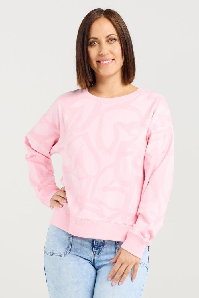 Woman wearing a pink sweater and light blue jeans on a plain background