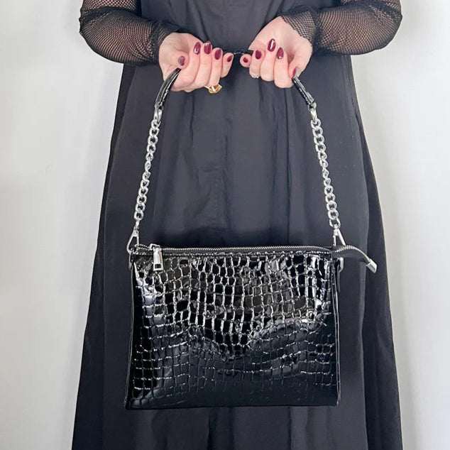 Person holding a black crocodile-patterned handbag against a plain background