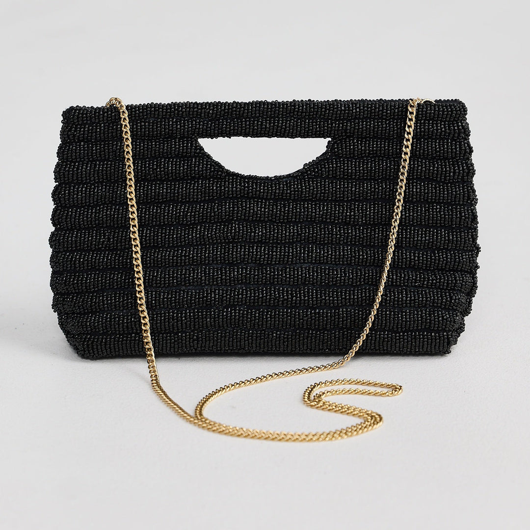 Black woven handbag with a gold chain strap on a light gray background