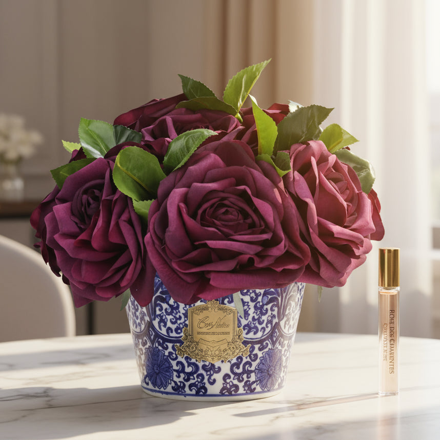 Bouquet of purple cote noire peonies in a decorative pot with a small bottle next to it. Peonies diffuser fragarnce just like a reed diffuser.