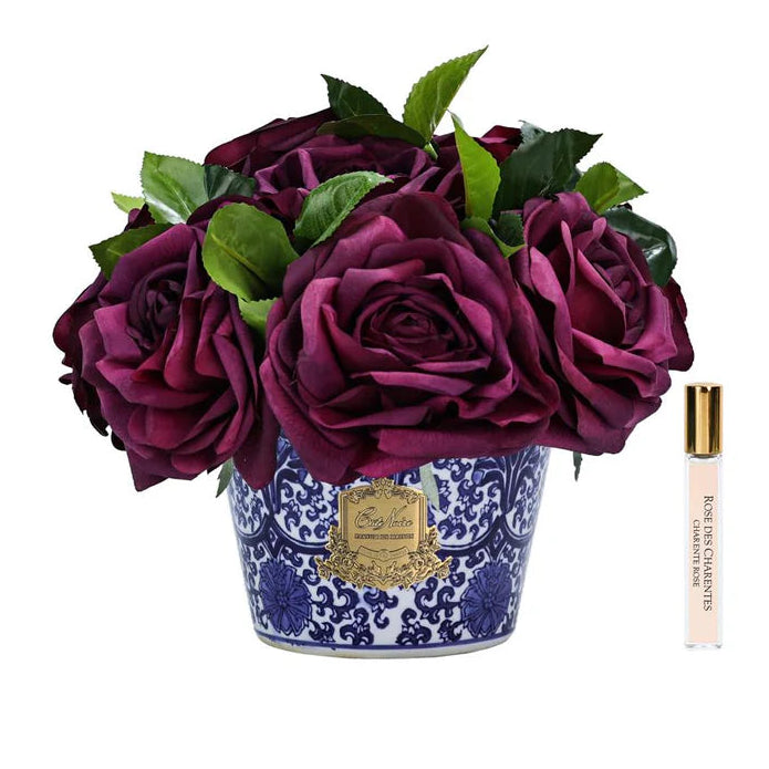 Bouquet of purple cote noire peonies in a decorative pot with a small perfume bottle on a white background