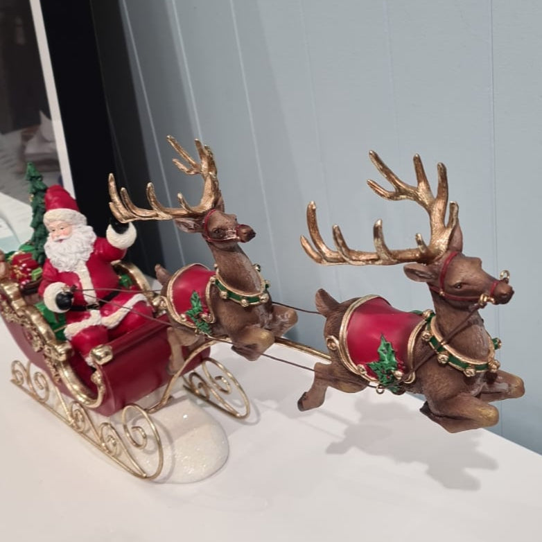 Decorative Christmas scene with Santa in a sleigh pulled by reindeer on a white surface.