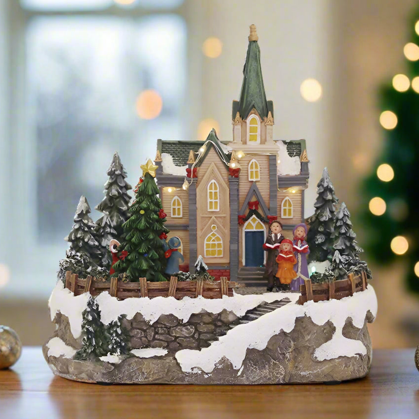 Decorative Christmas village scene with a church, trees, and people on a white background.