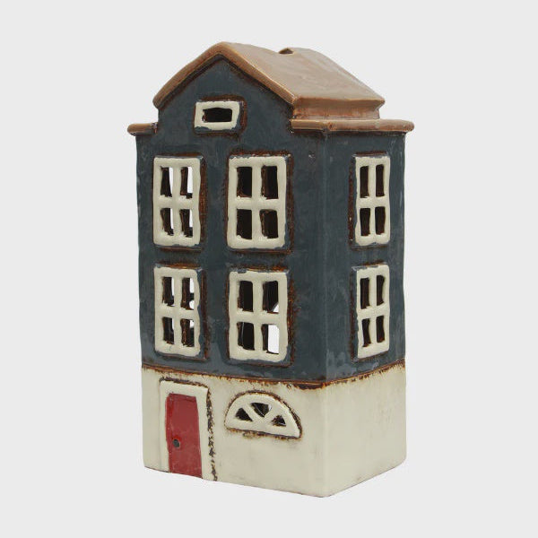 Ceramic house-shaped container with a blue body, brown roof, and red door on a light gray background.
