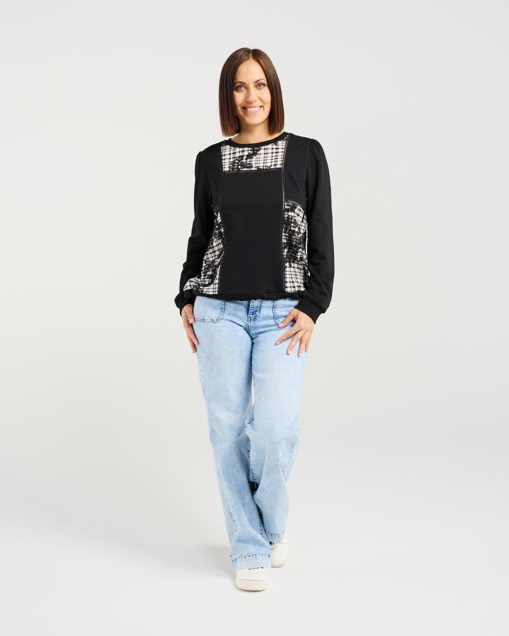 Woman wearing a black and white patterned top with light blue jeans on a white background