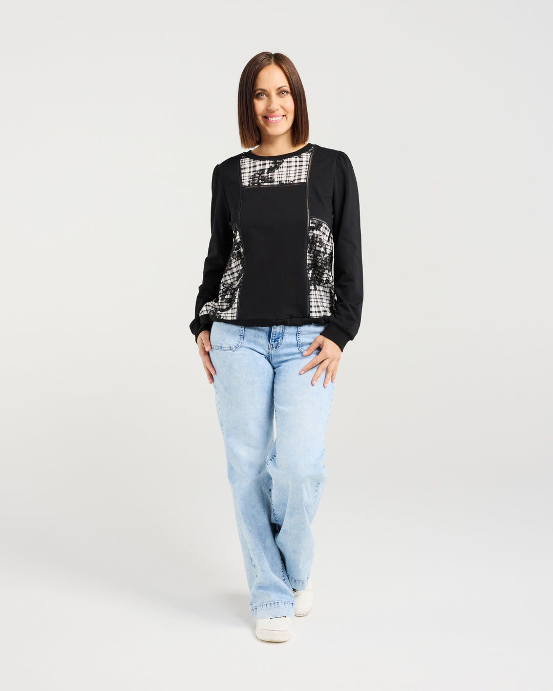 Woman wearing a black and white patterned top with light blue jeans on a white background