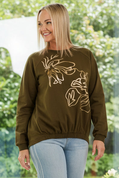 Woman wearing an olive green sweatshirt with a graphic design and light blue jeans on a white background