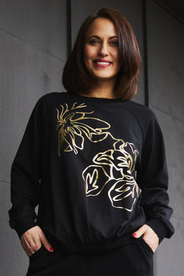 Woman wearing a black sweatshirt with floral design against a dark wall.