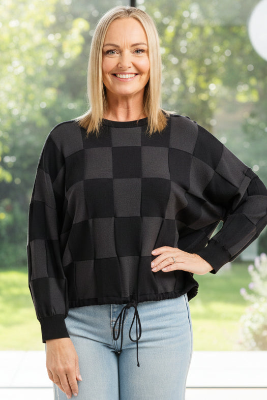 Woman wearing a black and gray checkered sweater and light blue jeans on a white background