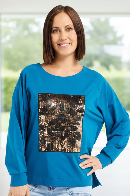 Woman wearing a blue sweater with a graphic design and light blue jeans on a white background