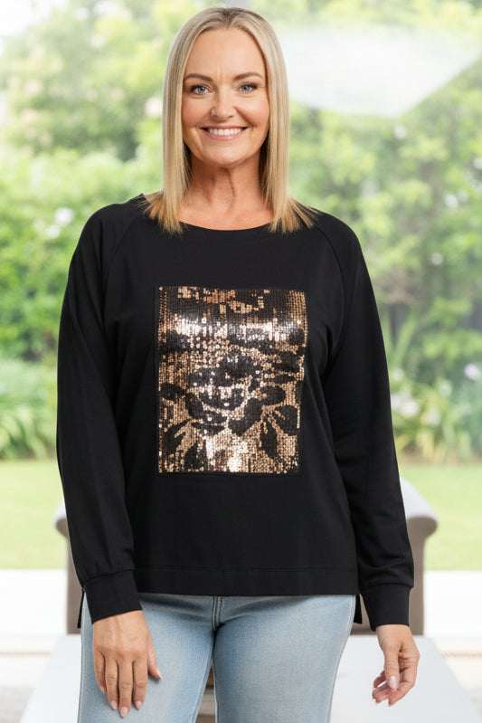 Woman wearing a black long-sleeve top with a gold pattern and light blue jeans on a white background