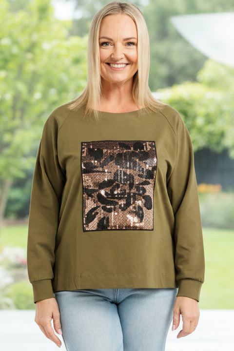 Woman wearing an olive green sweatshirt with a graphic design and light blue jeans on a white background