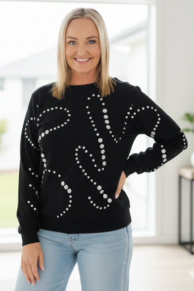 Woman wearing a black sweater with white patterns and light blue jeans on a white background