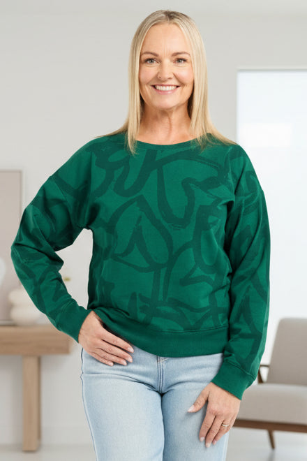 Woman wearing a green patterned sweater and light blue jeans on a white background