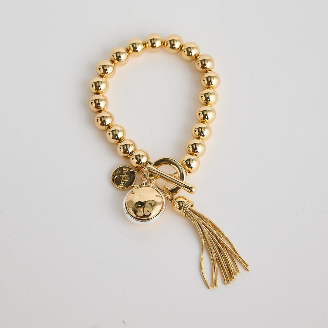 Gold beaded bracelet with tassel charm on a light gray background