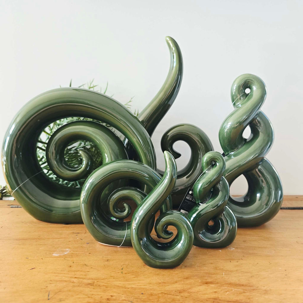 A glossy dark green sculptural decorative piece with multiple curled spiral and loop shapes, displayed on a wooden surface against a plain light background.
