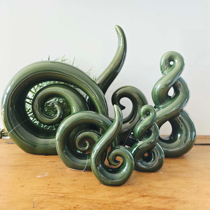 A glossy dark green sculptural decorative piece with multiple curled spiral and loop shapes, displayed on a wooden surface against a plain light background.