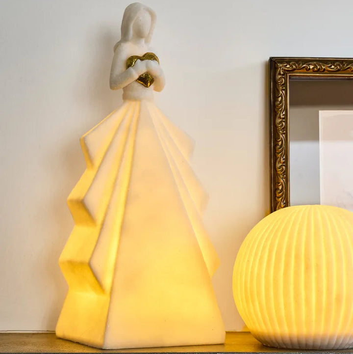 Decorative lamp shaped like a woman with a yellow light, next to a spherical lamp on a shelf.