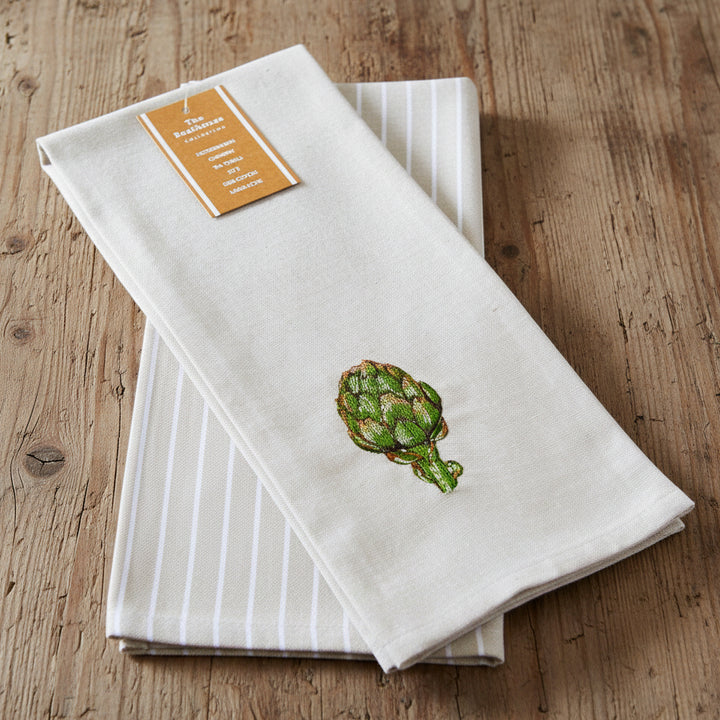 A folded beige kitchen towel with white vertical stripes and a green embroidered artichoke, featuring a tan paper label at the top.