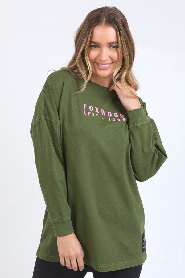 Woman wearing a green long-sleeve shirt with 'Foxwood' text on a white background