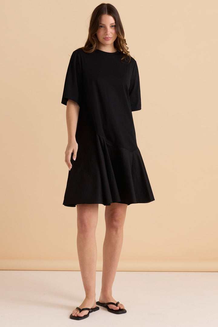 Woman wearing a black betty basics cassidy knee length dress against a beige background