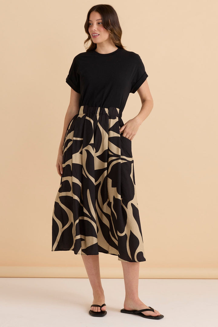 Woman wearing a black Betty Basics Ayden t-shirt dress with black & beige patterned skirt against a beige background